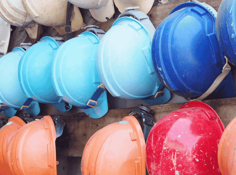 A collection of colourful hard hats hanging on a wall.