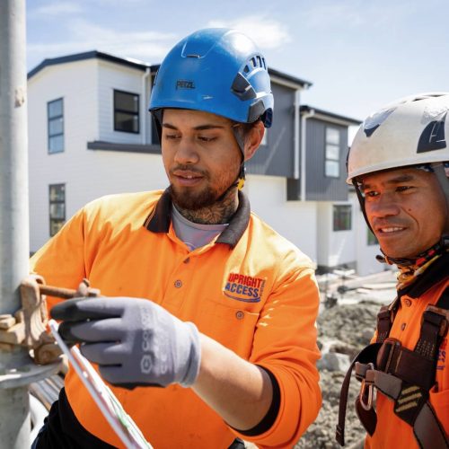 Two scaffolders in safety helmets and hi-vis clothing assembling scaffolding on a construction site.
