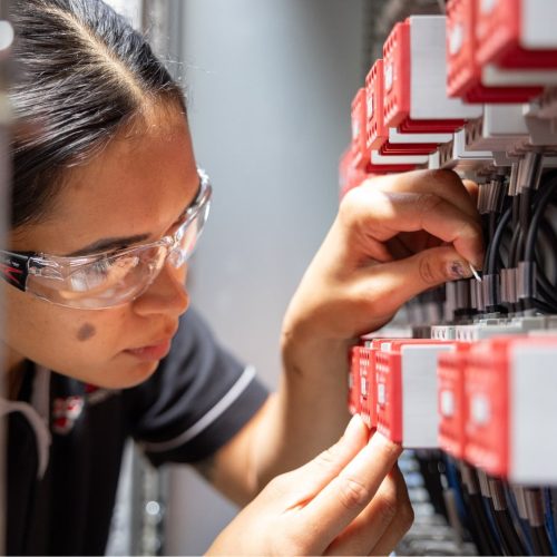 Apprentice electrician wearing safety glasses carefully wiring components inside an electrical panel.