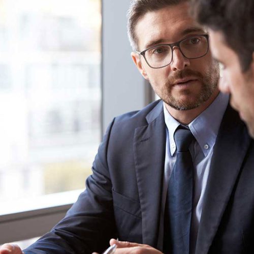 Business professional in a suit speaking with a colleague during a meeting.