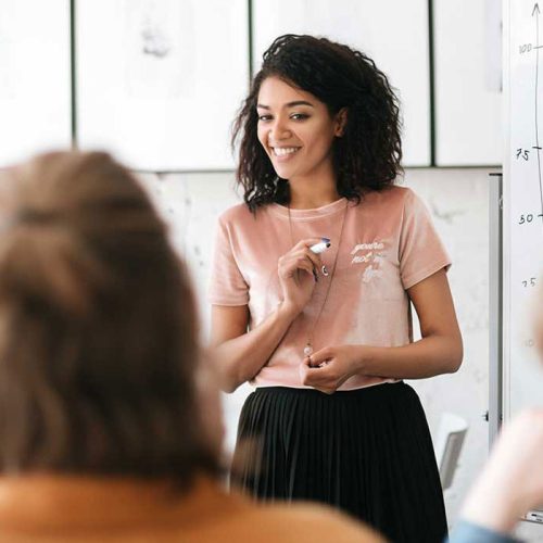 Smiling project manager leading a discussion and presenting ideas on a whiteboard.