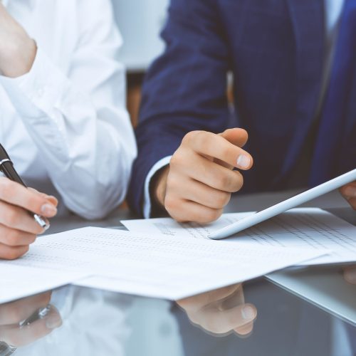 Two professionals reviewing financial documents and data on a tablet at a desk.